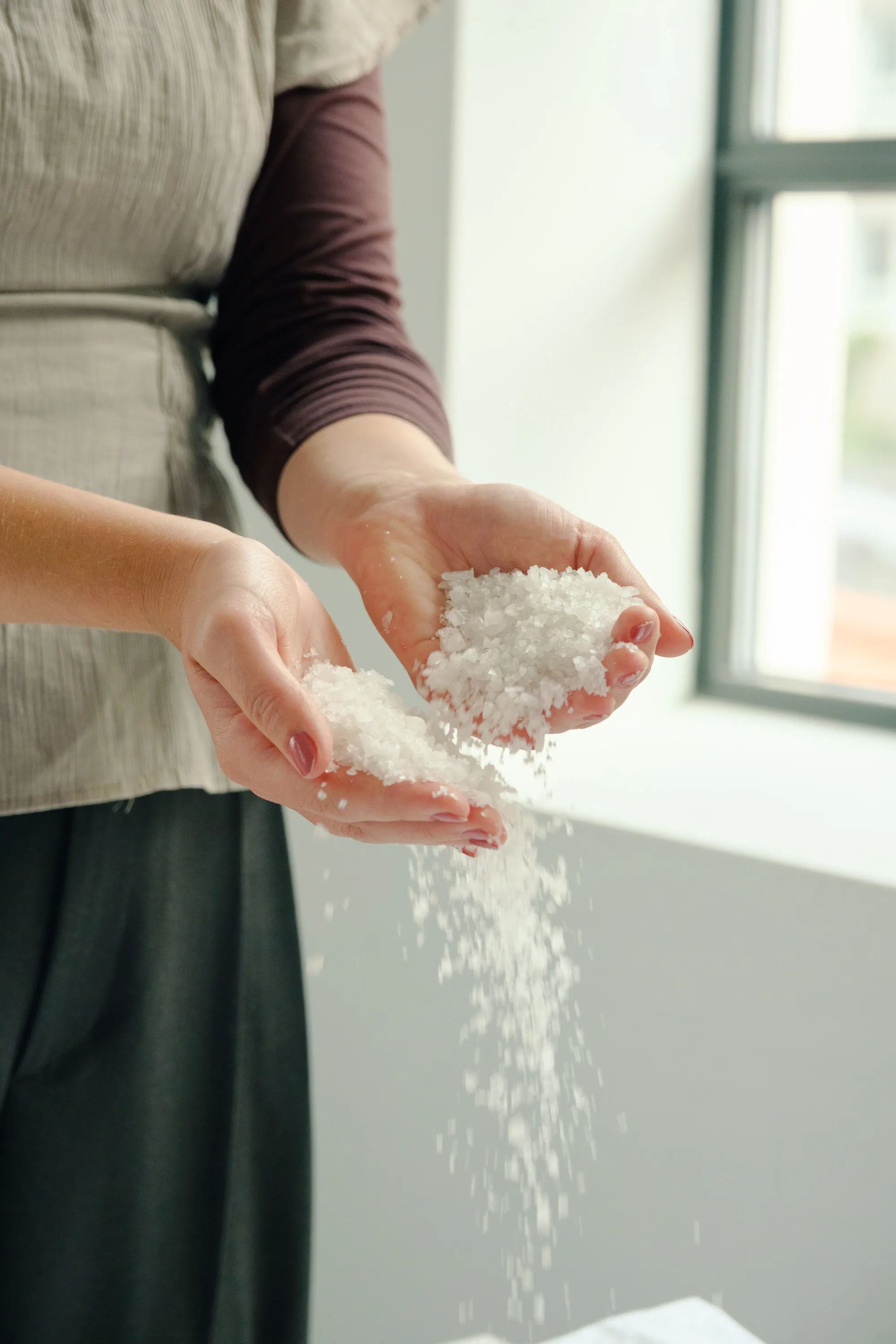 Hender som holder grovt hvitt salt som drysser mellom fingrene.
